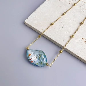 Macro detail of blue glass pendant with gold foil and 18K gold-plated beaded chain