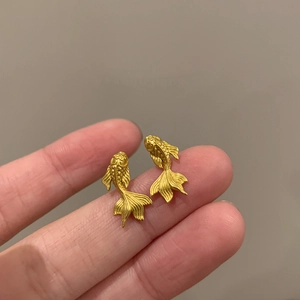 Boucles d'oreilles carpe koï plaquées or 18K montrant la taille mini sur le bout des doigts