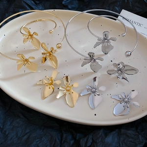 Detailed close-up of metallic flower earrings in gold and silver finish on a ceramic tray