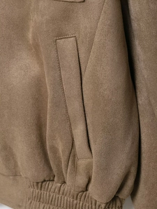 Detailed view of dark brown suede jacket featuring stitching and ribbed elastic hem