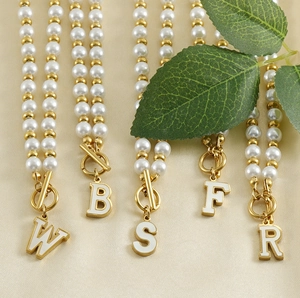 Détail de colliers de perles dorés 18K avec fermoir OT et pendentifs lettres sur soie