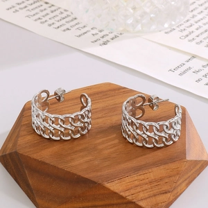 Detail of silver hollow chain hoop earrings on a hexagonal wooden base with vintage paper