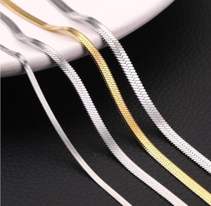 Primer plano de cadenas de serpiente planas en oro y plata de varios anchos sobre negro