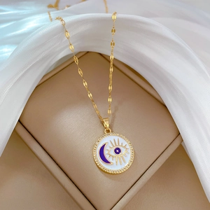 Detailed close-up of golden eye and moon enamel necklace displayed on a luxury jewelry box