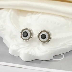 Macro shot of silver evil eye stud earrings on a white relief base and cream silk