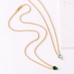 Detail of golden tennis chains with pear-cut green and light blue zircon pendants