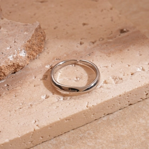 Detailed view of a silver geometric irregular open ring on a textured stone surface