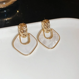 Detailed shot of gold hammered metal earrings with white acrylic diamond-shaped pendants