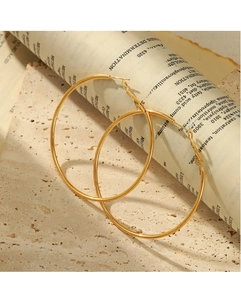 Detailed view of large gold stainless steel hoop earrings on stone and newspaper background