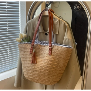 Detail of woven straw tote bag with brown PU leather straps and stylish tassel charm