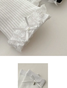 Detail of white cotton knit socks with lace trim, bow, and metal heart pendant