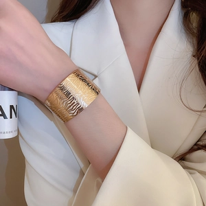 Detail of wide golden geometric cuff bracelet with textured wave pattern on a model