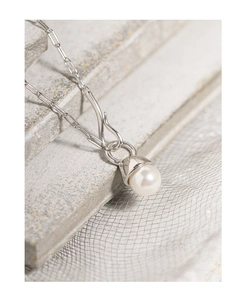 Macro shot of silver paperclip chain necklace with a white pearl pendant on stone