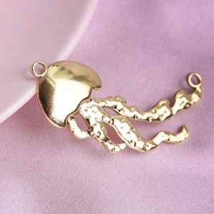 Detailed view of golden jellyfish pendant with hammered texture on pink fabric background