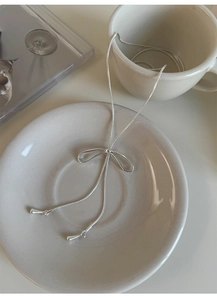 Dettaglio ravvicinato di una collana a fiocco d'argento con nappe su piatto bianco