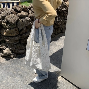 Outdoor shot of a white floral lace canvas tote bag showing textured detail and side profile