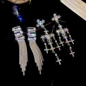 Macro detail of silver cross earrings with dangling pearls and crystal tassels