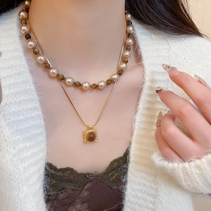 Detail of layered tiger eye pearl necklace and square pendant on a white cardigan