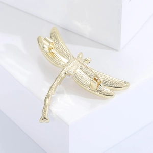 Detailed view of a golden dragonfly brooch with engraved wings on a white pedestal