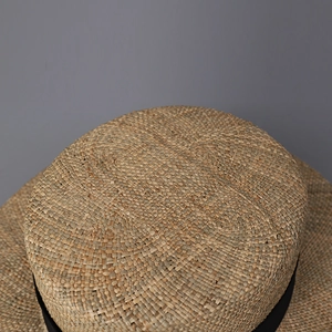 Close-up of hand-woven boater hat showing detailed straw texture and black ribbon