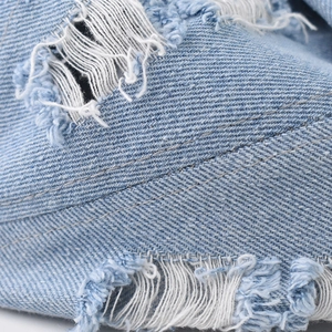 Detailed macro view of distressed light blue denim fabric with white frayed rips and texture