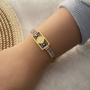 Detail of gold evil eye bracelet with coin charm and baguette zircon links on wrist