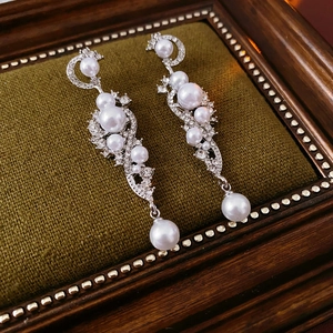 Detailed view of silver wheat pearl earrings with diamonds on green velvet display
