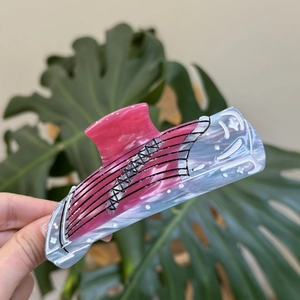 Vioolvormige haarklem van roze en blauw gemarmerd acetaat bij een groen blad