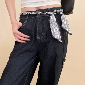 Détail d'un jean en denim bleu foncé avec une ceinture en soie à motif cachemire noir et blanc