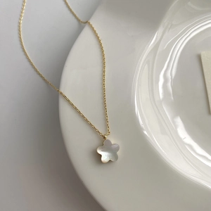 Macro detail of gold necklace with white mother-of-pearl flower pendant on ceramic