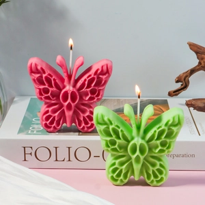 Candele profumate a farfalla rosa e verde con ali traforate su libri vintage