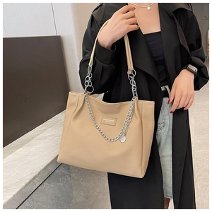 Close-up of a khaki tote bag with a decorative silver chain shown on a model side-profile