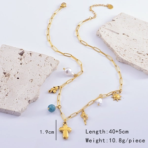 Detail of gold ocean-themed necklace with shell, cross and pearl charms on stone