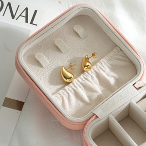 Close-up of golden teardrop stud earrings with mirror finish on pink velvet jewelry box