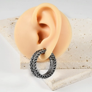 Detail of vintage silver textured ear gauge on a silicone ear model over stone props