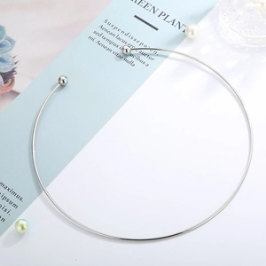 Close-up of minimalist silver stainless steel torque choker with spherical ends on a desk