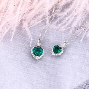 Detail of heart-shaped emerald green gemstone pendant with diamond halo on silver chain