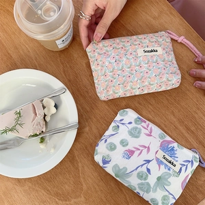 Dettaglio di pochette floreali in tela con cerniera e cinturino su tavolo in legno