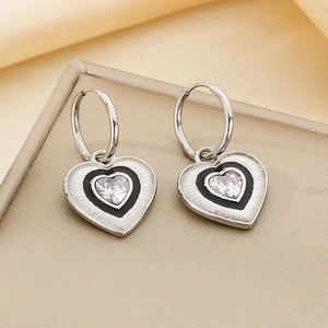 Close-up of heart earrings with black enamel and sparkling zircon on silk background