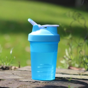 Detail of blue fitness shaker bottle with scale on outdoor grass background