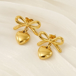 Boucles d'oreilles nœud et cœur en acier inoxydable doré sur tissu de soie blanc