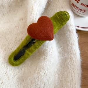 Close-up of heart-shaped hair clip with green woven texture and red wool heart
