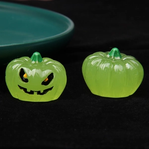 Close-up of two small green luminous resin pumpkins on black velvet for Halloween decor