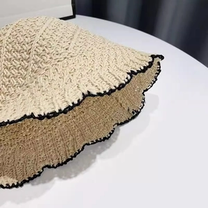 Detail shot of the beige straw bucket hat showing intricate weaving and black wavy edge