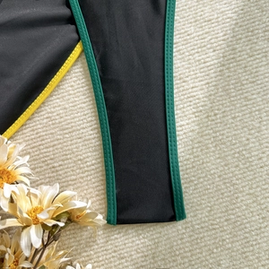 Detail of high-elastic black bikini with green and yellow piping on white plush background