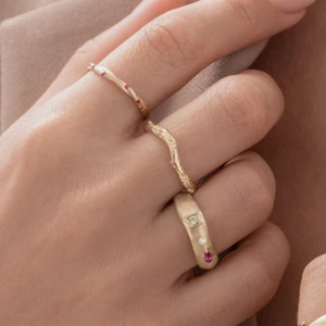 Detailed view of textured gold rings set with colorful gemstones on a model's hand