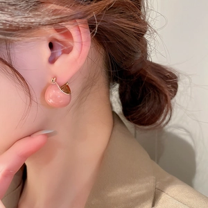 Close-up of pink drip oil bean earring worn by a model in a warm setting