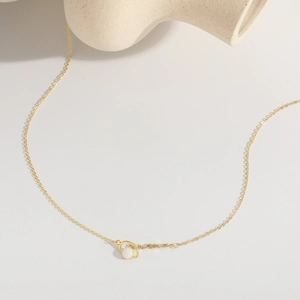 Close-up of gold MAMA necklace with opal gemstone on a minimalist white surface