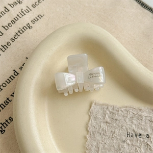 Detailed macro view of an ivory acetate bow hair claw with pearlescent finish in a dish