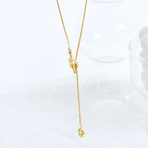 Detailed close-up of golden knot pendant on a y-shaped snake chain sweater necklace